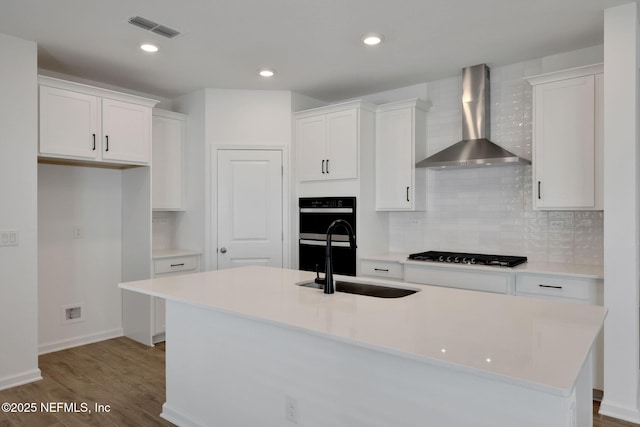 kitchen featuring wall chimney range hood, sink, an island with sink, and white cabinets