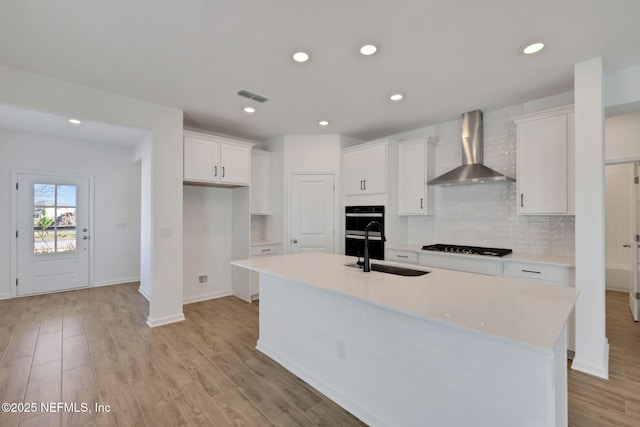 kitchen featuring sink, light hardwood / wood-style flooring, white cabinetry, an island with sink, and wall chimney exhaust hood