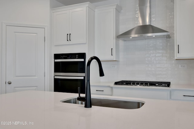 kitchen with wall chimney exhaust hood, sink, double oven, and white cabinets