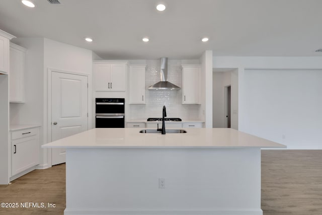 kitchen featuring white cabinetry, sink, a kitchen island with sink, and wall chimney range hood