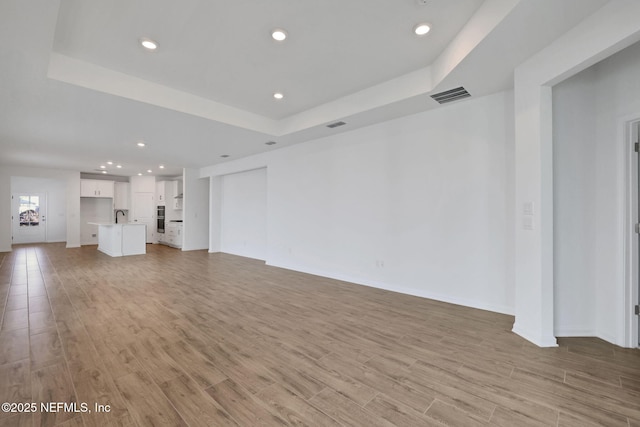 unfurnished living room featuring sink, light hardwood / wood-style floors, and a tray ceiling