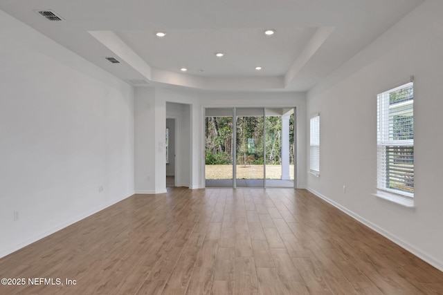 empty room with light wood-type flooring and a tray ceiling