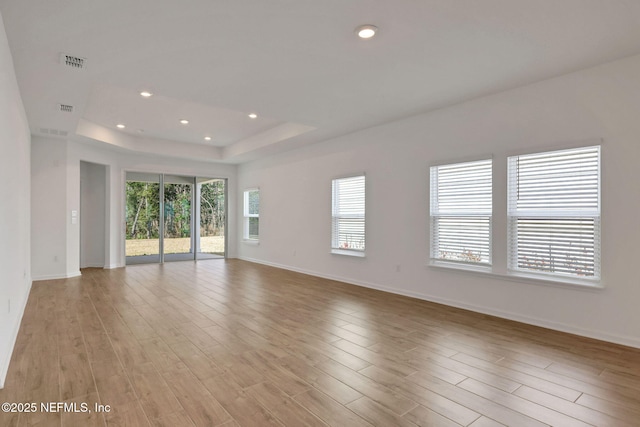 spare room with a raised ceiling and light hardwood / wood-style floors