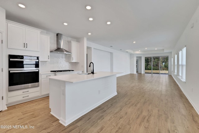 kitchen with white cabinetry, wall chimney exhaust hood, sink, and an island with sink