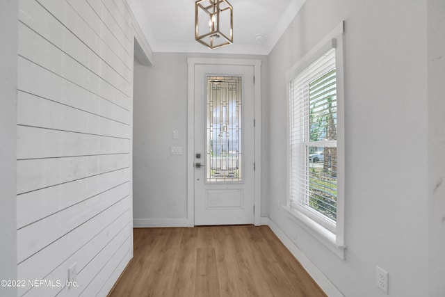 entryway featuring an inviting chandelier, a wealth of natural light, ornamental molding, and light wood-type flooring