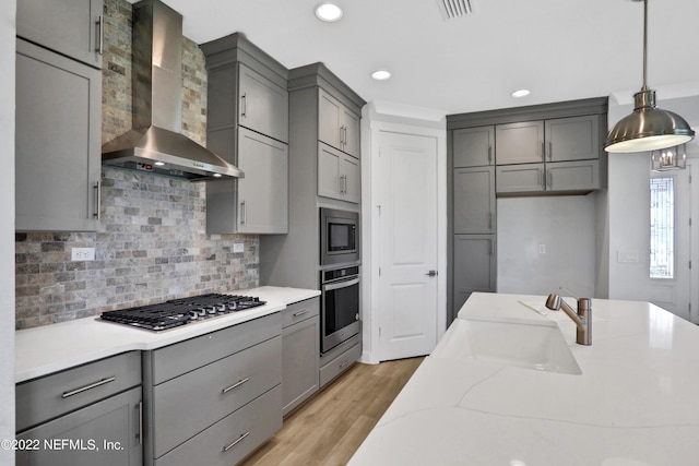 kitchen featuring decorative light fixtures, wall chimney range hood, stainless steel appliances, sink, and gray cabinetry