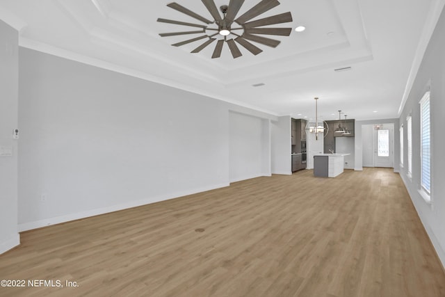 unfurnished living room with ceiling fan, a raised ceiling, ornamental molding, and light hardwood / wood-style flooring