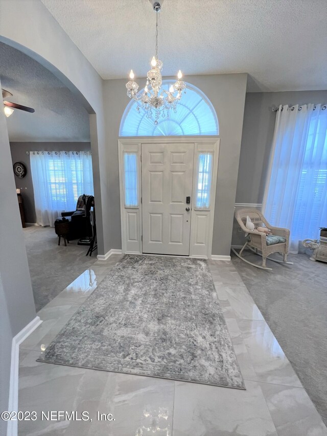 entrance foyer featuring a textured ceiling, light colored carpet, and ceiling fan with notable chandelier