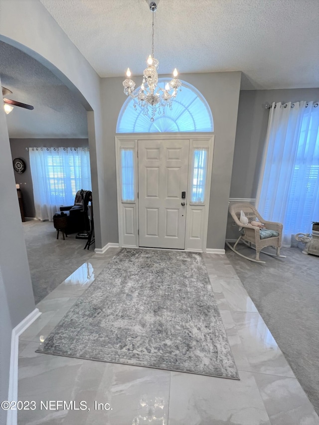 entrance foyer with arched walkways, baseboards, ceiling fan, marble finish floor, and a textured ceiling