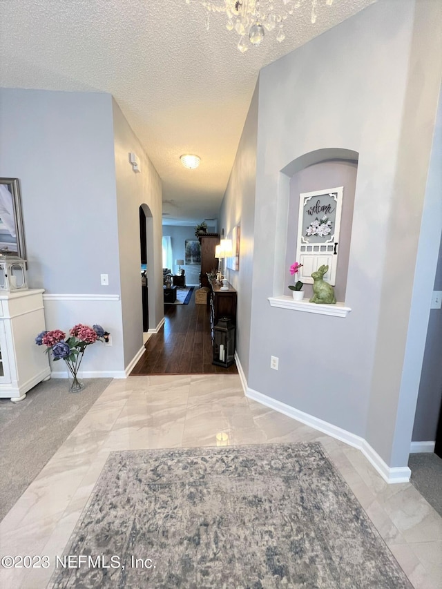 corridor featuring an inviting chandelier, a textured ceiling, and tile patterned flooring