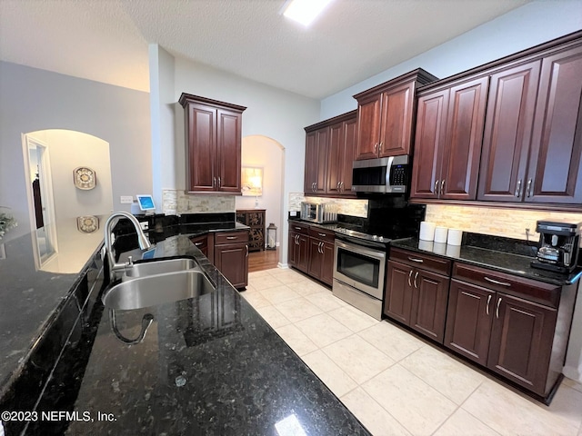 kitchen featuring arched walkways, light tile patterned floors, decorative backsplash, appliances with stainless steel finishes, and a sink