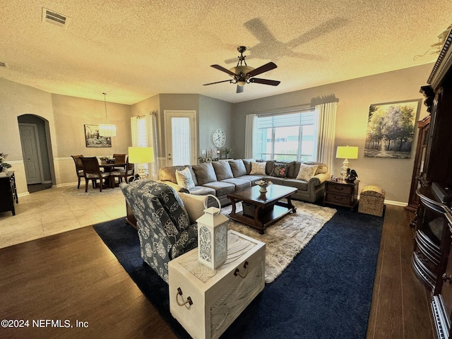 living area with arched walkways, visible vents, light wood-style flooring, and a textured ceiling