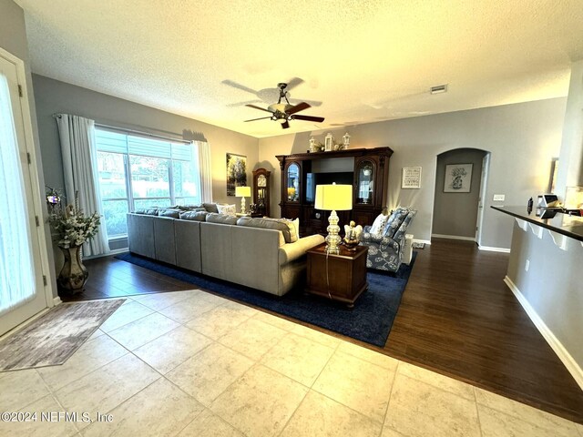 living area featuring baseboards, visible vents, arched walkways, ceiling fan, and a textured ceiling