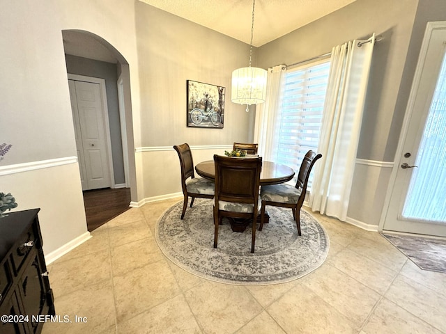 dining area featuring baseboards, arched walkways, a chandelier, and tile patterned floors