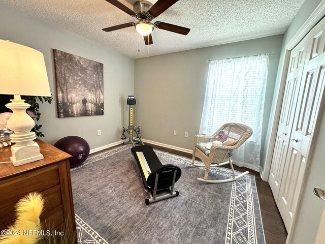 workout room with a textured ceiling, dark wood-style flooring, a ceiling fan, and baseboards