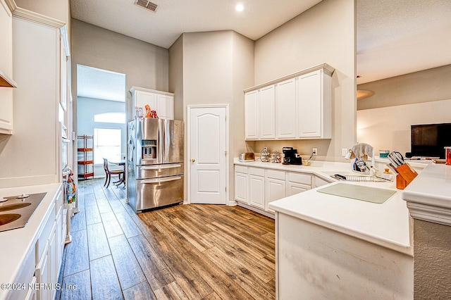 kitchen with a peninsula, electric cooktop, wood finished floors, white cabinets, and stainless steel fridge with ice dispenser