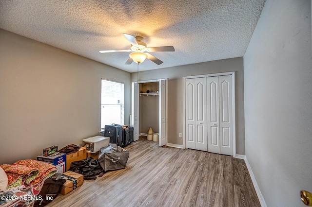 unfurnished bedroom featuring baseboards, a textured ceiling, light wood finished floors, and two closets