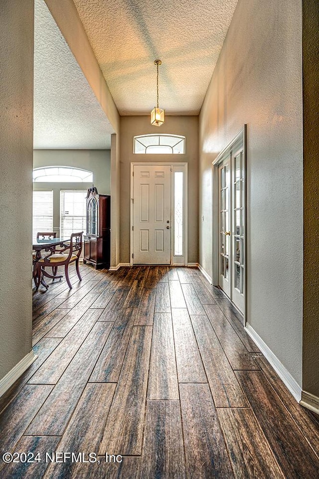 foyer featuring a textured ceiling, a textured wall, baseboards, french doors, and hardwood / wood-style floors