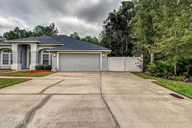 ranch-style house with driveway, an attached garage, a gate, and fence