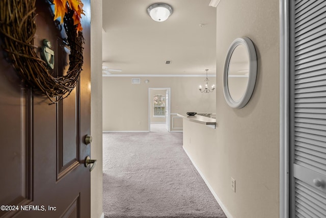 hall with carpet flooring, crown molding, and an inviting chandelier