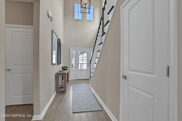 foyer entrance with light wood-type flooring, a high ceiling, and an inviting chandelier