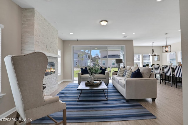 living room with a chandelier, hardwood / wood-style floors, and a stone fireplace