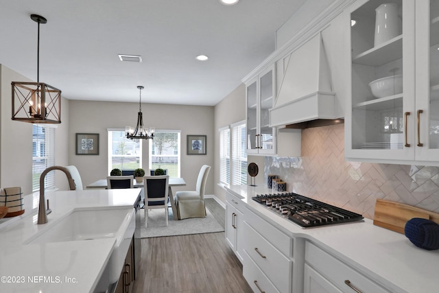 kitchen with custom exhaust hood, decorative light fixtures, white cabinetry, a chandelier, and stainless steel gas stovetop