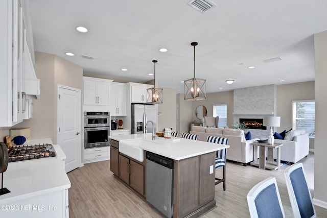 kitchen with light hardwood / wood-style floors, stainless steel appliances, a kitchen island with sink, pendant lighting, and white cabinets