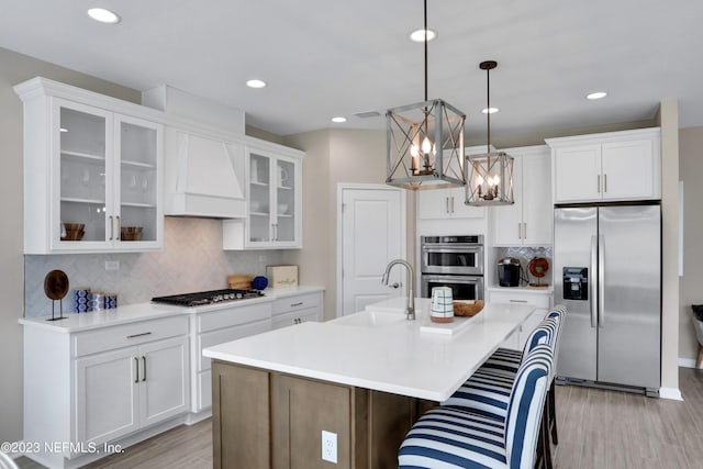 kitchen with a center island with sink, stainless steel appliances, hanging light fixtures, custom range hood, and sink