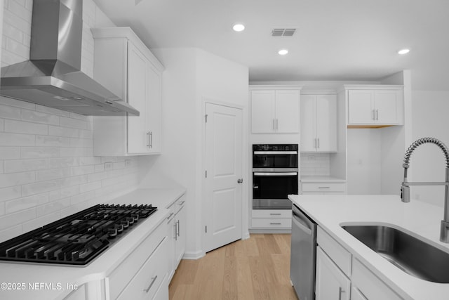 kitchen with gas stovetop, sink, white cabinets, and wall chimney exhaust hood