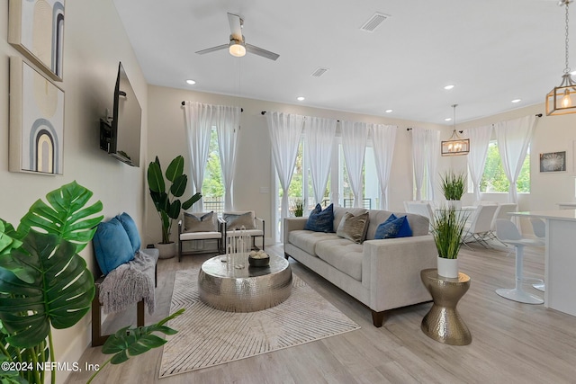 living room featuring light hardwood / wood-style floors, a wealth of natural light, and ceiling fan with notable chandelier