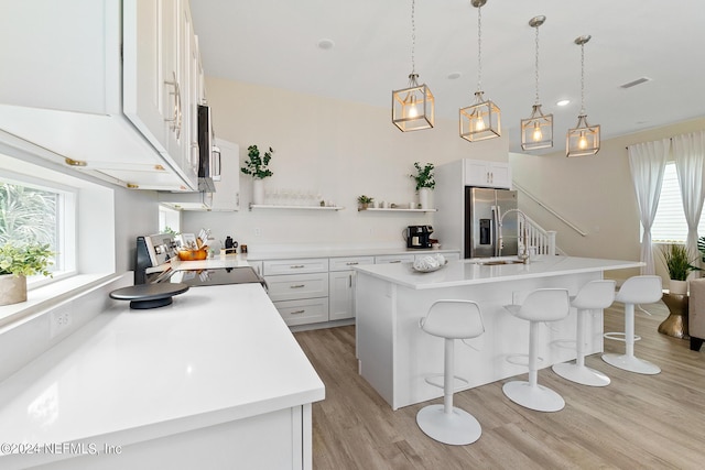 kitchen with decorative light fixtures, an island with sink, white cabinetry, appliances with stainless steel finishes, and a kitchen breakfast bar