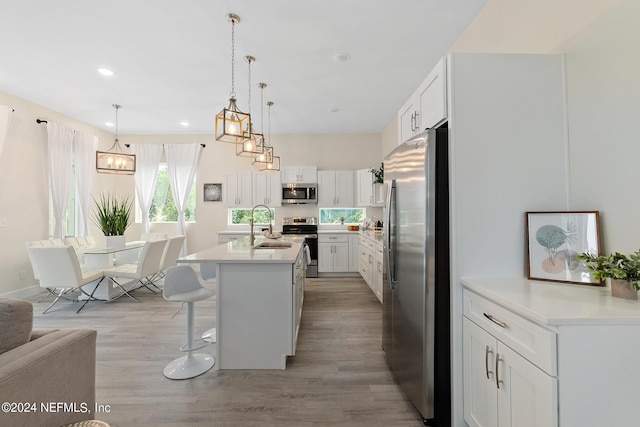 kitchen with a breakfast bar area, appliances with stainless steel finishes, hanging light fixtures, an island with sink, and white cabinetry