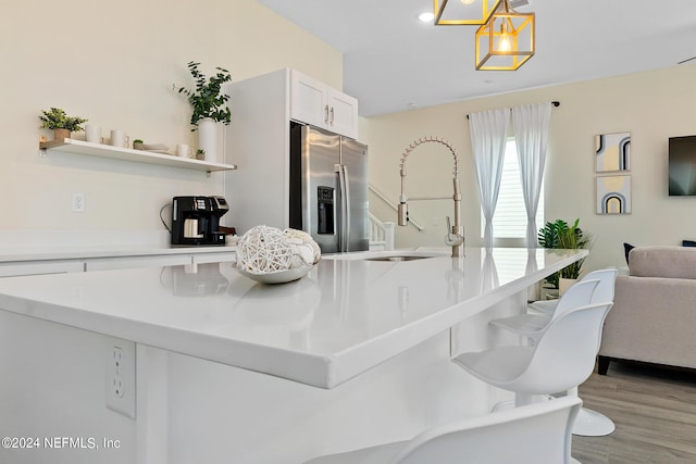 kitchen featuring white cabinetry, pendant lighting, stainless steel refrigerator with ice dispenser, sink, and light hardwood / wood-style flooring