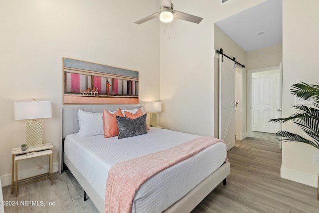 bedroom with hardwood / wood-style flooring, ceiling fan, a barn door, and a closet