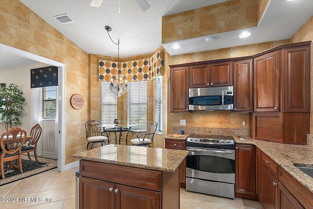 kitchen featuring ceiling fan with notable chandelier, hanging light fixtures, appliances with stainless steel finishes, light tile patterned flooring, and light stone counters