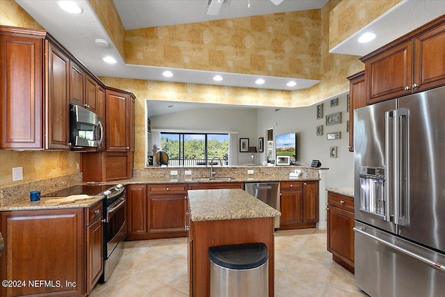 kitchen featuring kitchen peninsula, appliances with stainless steel finishes, light stone countertops, sink, and a kitchen island