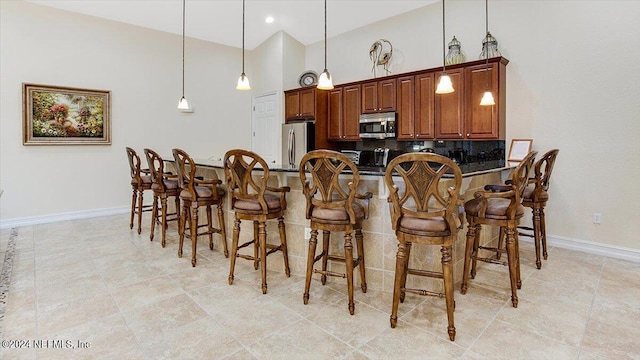 kitchen featuring backsplash, kitchen peninsula, decorative light fixtures, a breakfast bar, and appliances with stainless steel finishes