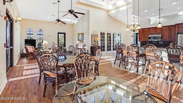 dining area featuring french doors, ceiling fan with notable chandelier, wood-type flooring, and a high ceiling