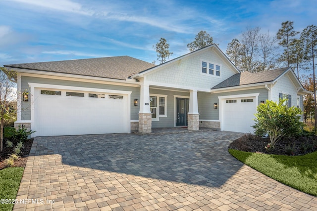 view of front of house with stone siding, decorative driveway, a shingled roof, and an attached garage