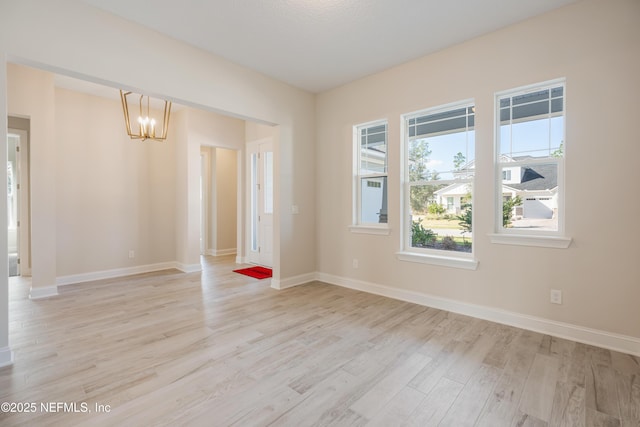 empty room with a notable chandelier, light wood finished floors, and baseboards