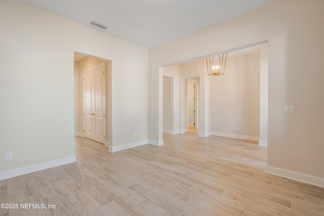 empty room featuring light wood-style floors, baseboards, visible vents, and an inviting chandelier