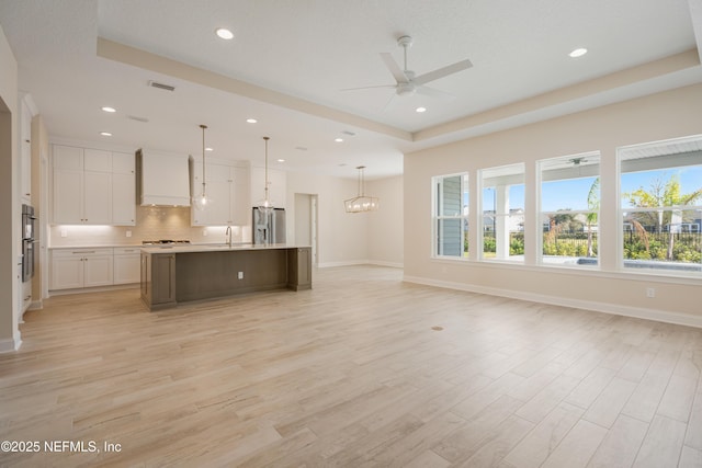 kitchen featuring open floor plan, custom exhaust hood, white cabinetry, stainless steel refrigerator with ice dispenser, and a sink