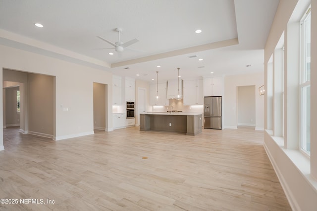 unfurnished living room featuring a raised ceiling, ceiling fan, sink, and light hardwood / wood-style flooring