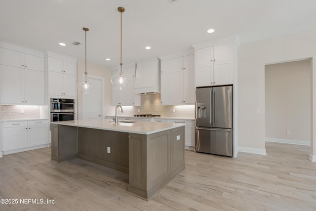 kitchen with stainless steel appliances, a sink, light countertops, decorative backsplash, and custom range hood