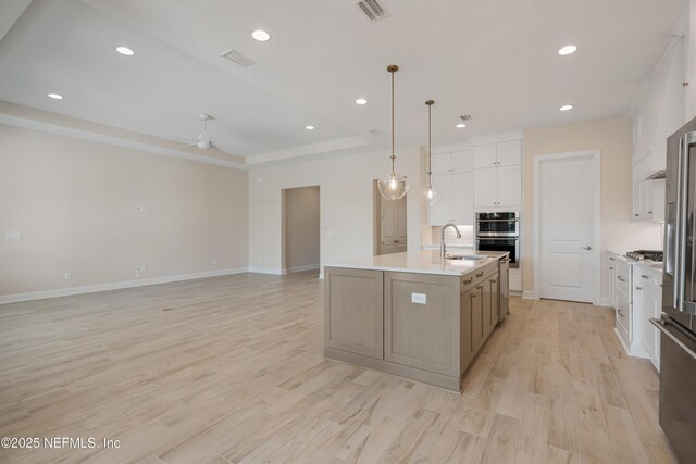 kitchen with ceiling fan, a spacious island, decorative light fixtures, white cabinets, and light wood-type flooring