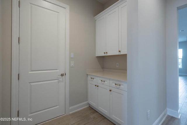 clothes washing area featuring light wood-style floors and baseboards