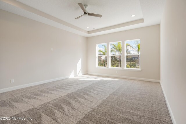 carpeted spare room featuring a tray ceiling and ceiling fan