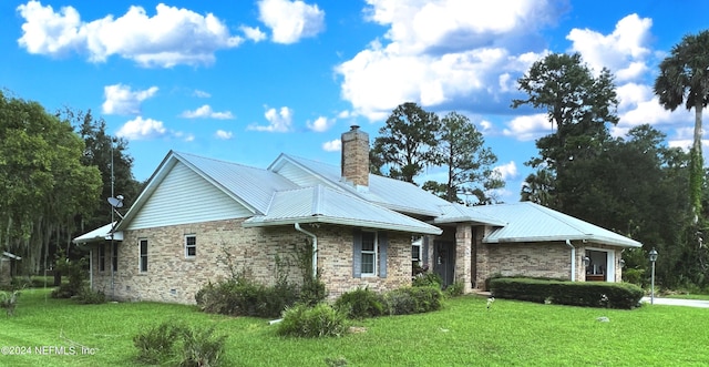 view of front facade with metal roof, a front lawn, a chimney, and brick siding