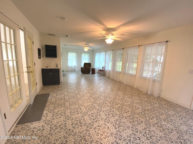 unfurnished living room with ceiling fan, visible vents, and speckled floor